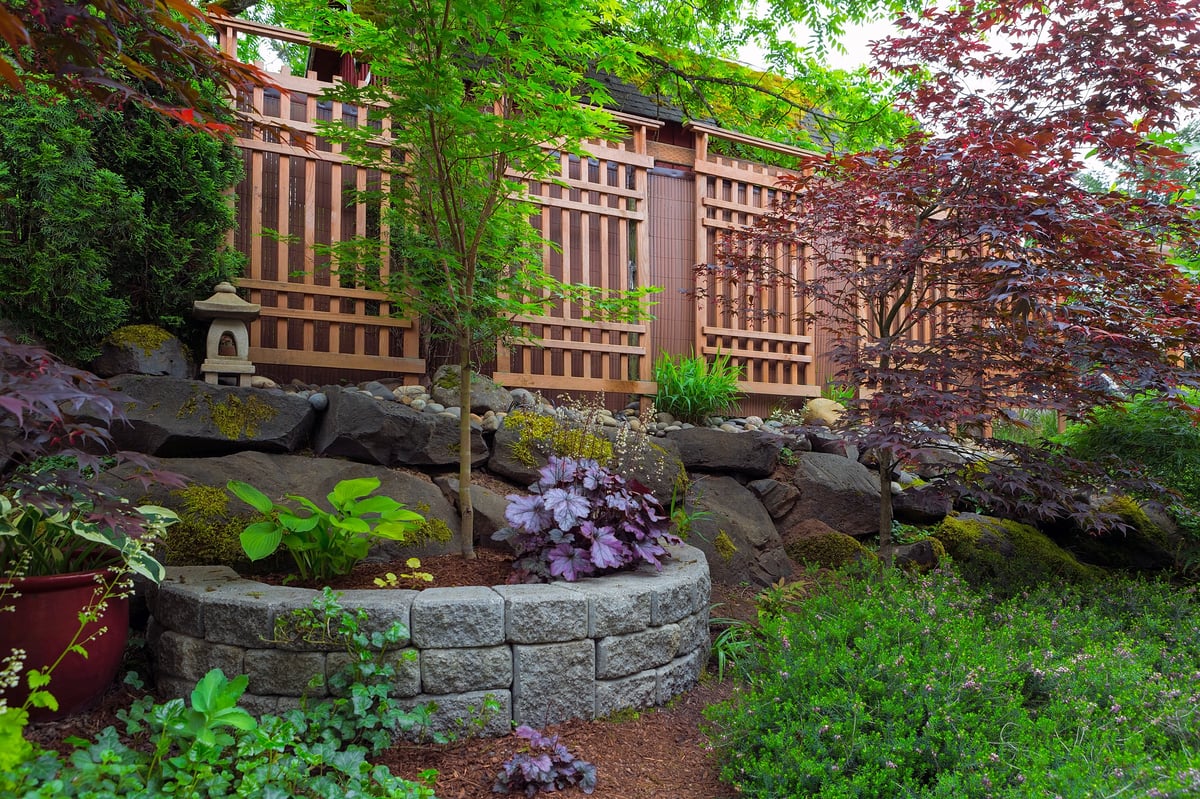 A home garden with natural and stone stacked planters, a trellis, lantern and shrubs