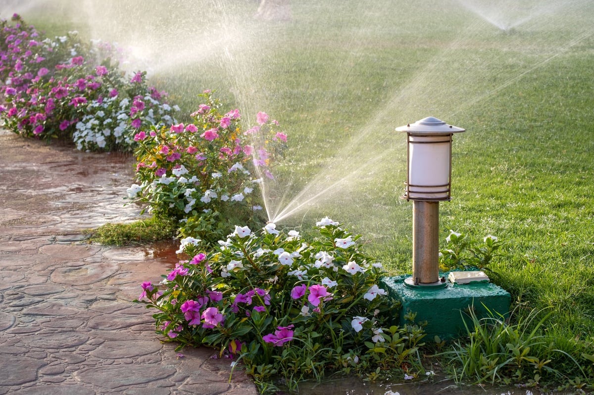 A sprinkler watering a flower bed on a green lawn in a summer garden