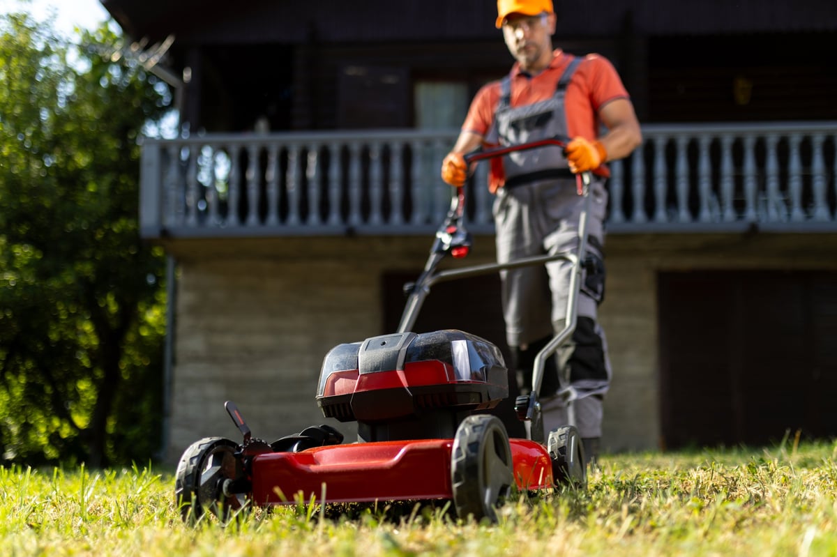 A gardener pushing a lawn mower across a lush green lawn