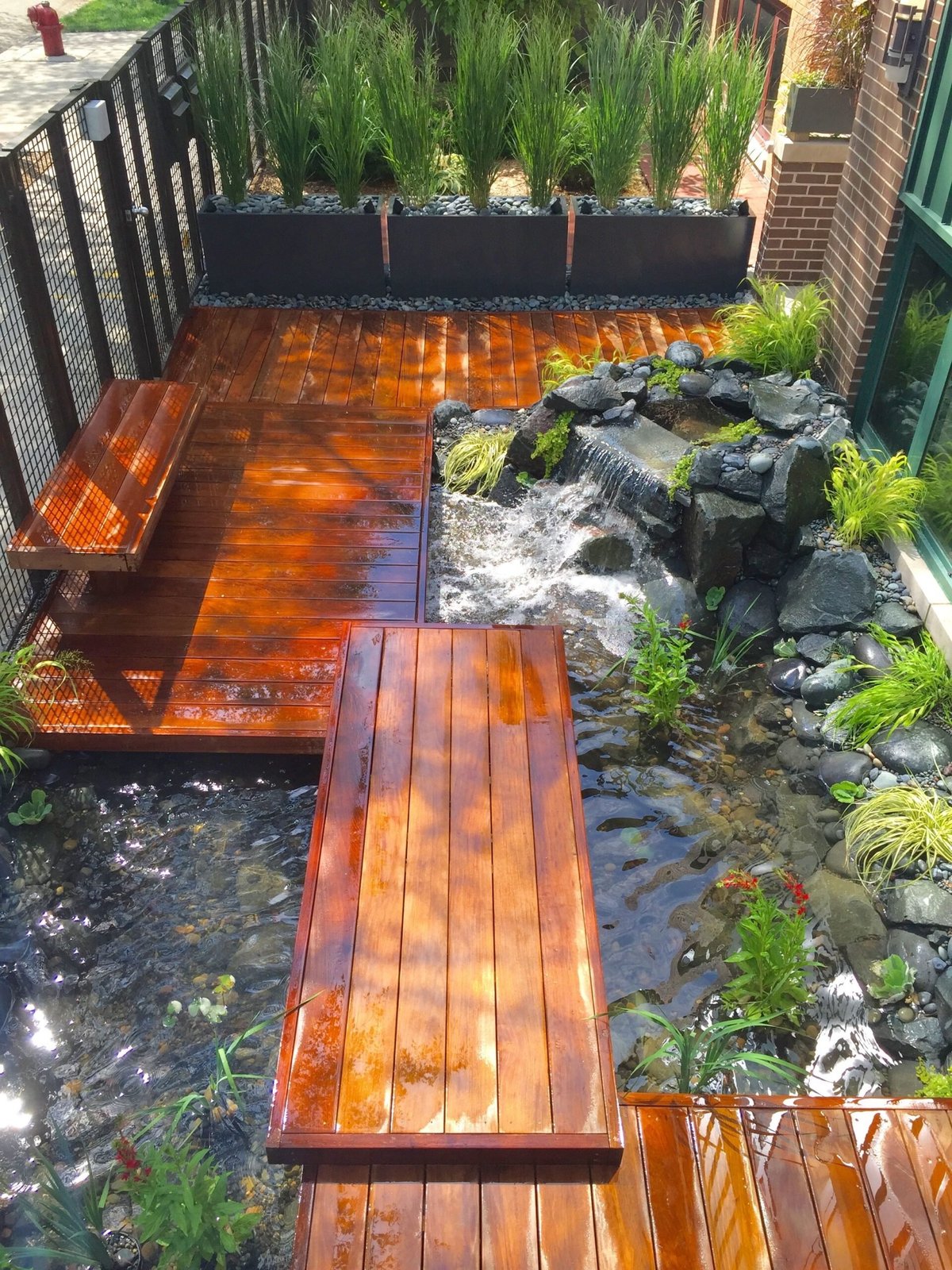 A wooden deck and boardwalk over a stream with large planters and rocks in a backyard garden