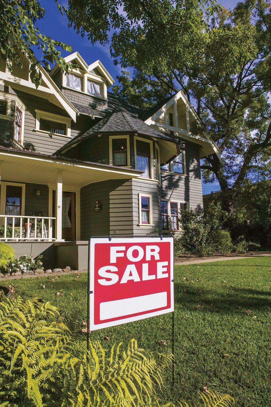 Two-story house with white trim and large front porch with a red For Sale sign in the yard