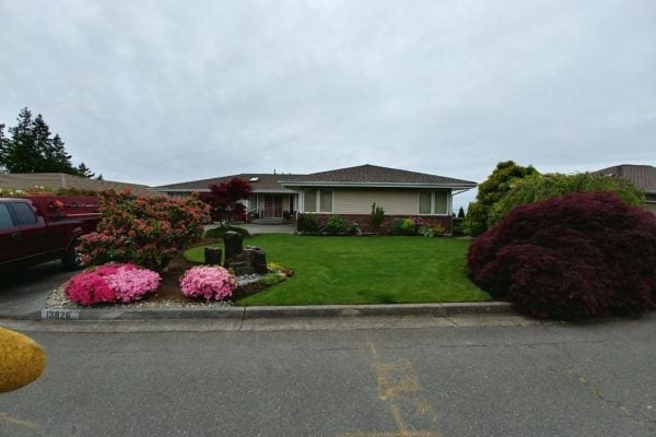 A single-story home with manicured landscaping, pink flowering shrubs and dark red foliage